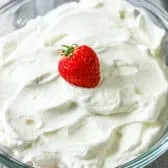 Whipped cream in a glass bowl with a strawberry on top